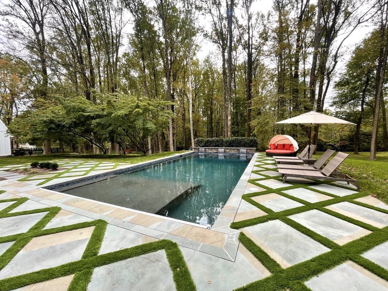 Modern geometric pool with turf inlay patio, built by Woodfield Outdoors for a custom backyard surrounded by mature trees.