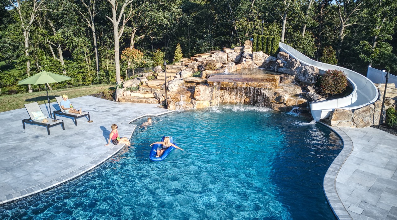 Family relaxing in and around a backyard pool built by Woodfield Outdoors, custom pool builders.
