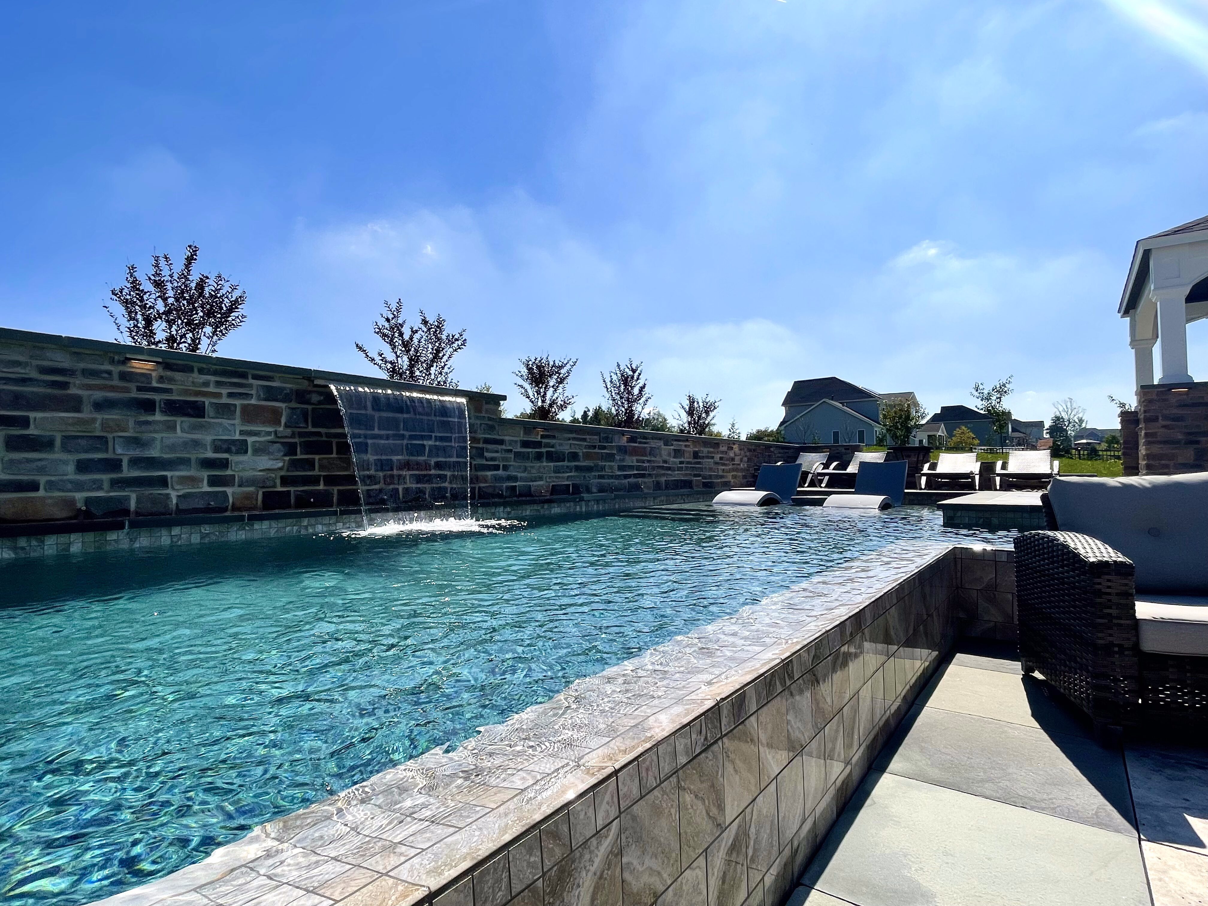 a rectangular swimming pool with an infinity edge, creating a seamless view of the turquoise water. The water laps over the near edge of the pool