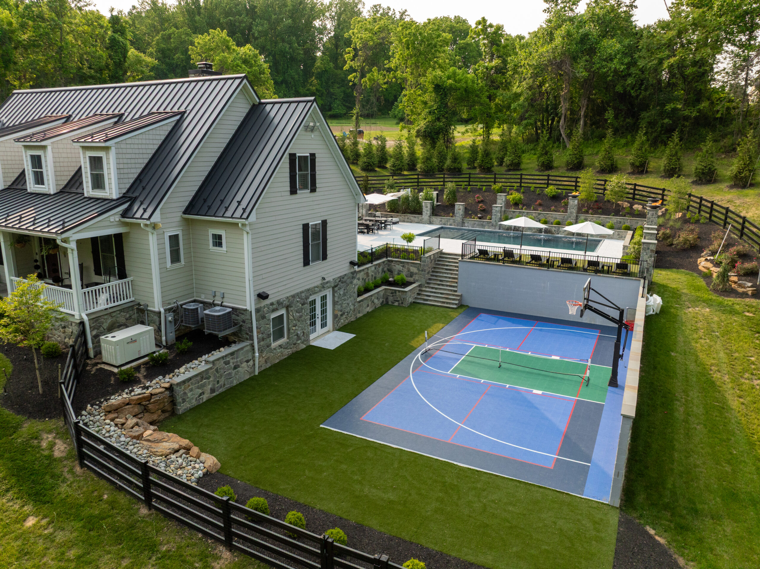 An aerial photo of a custom-designed backyard featuring a house, a swimming pool, and a multi-purpose sports court.